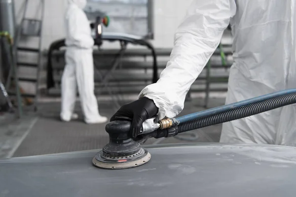 Cropped view of workman in hazmat suit polishing car in garage — Stock Photo