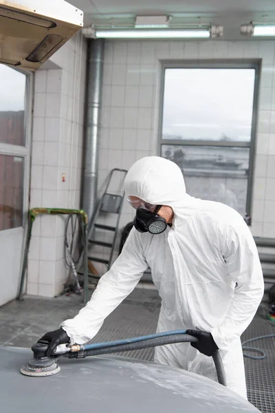 Foreman in protective suit polishing auto in garage — стокове фото