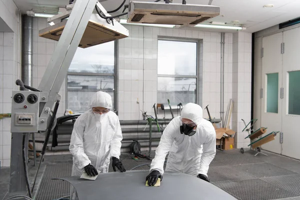 Mechaniker in Schutzanzügen arbeiten mit Schleifpapier und Motorhaube in der Garage — Stockfoto