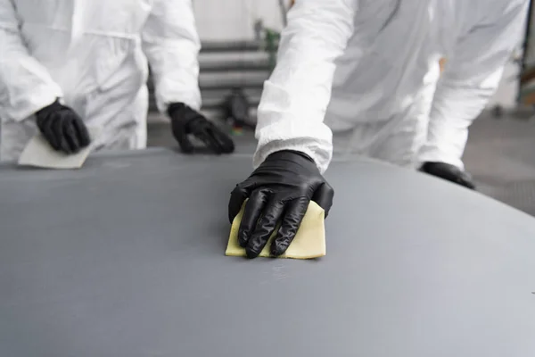 Cropped view of workman in protective suit working with sandpaper and car hood in garage — Fotografia de Stock