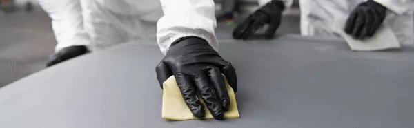 Cropped view of workman in hazmat suit and gloves using sandpaper on car hood in garage, banner — Stock Photo