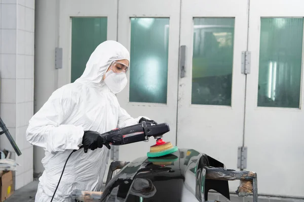 Arbeiterin im Schutzanzug poliert Autoteil im Einsatz — Stockfoto