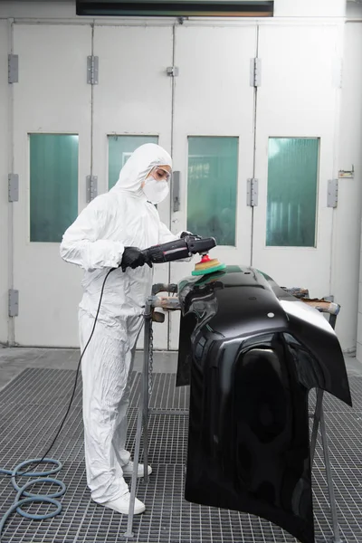 Workwoman in protective suit polishing car part in garage — Stockfoto