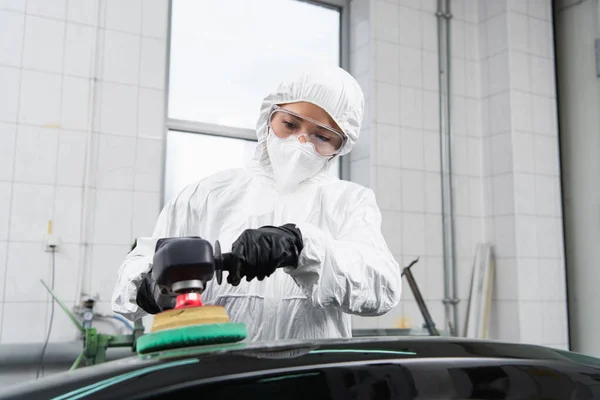 Trabajadora en traje de materiales peligrosos y máscara protectora pulido coche en servicio - foto de stock