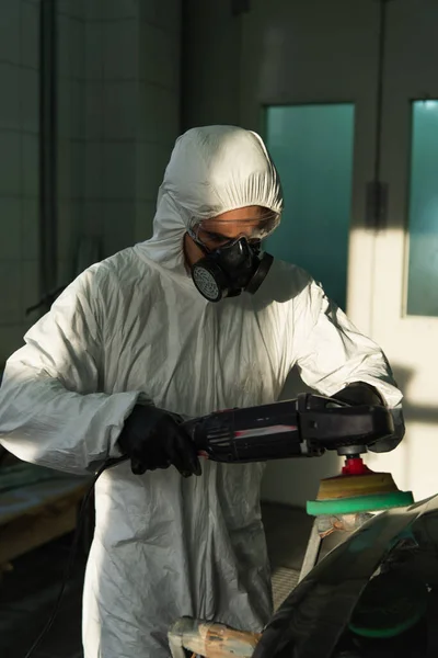 Workman in hazmat suit holding car polisher near part in garage — Stock Photo