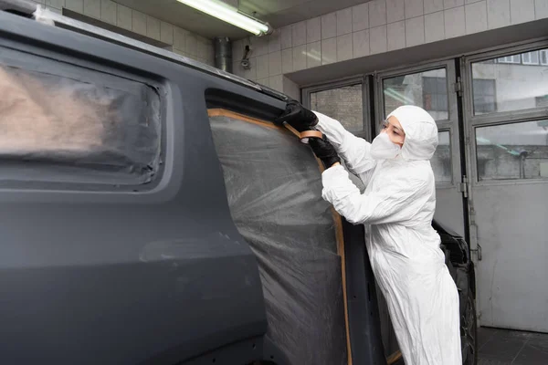 Trabajadora en traje de materiales peligrosos aplicando cinta adhesiva en el coche en servicio - foto de stock
