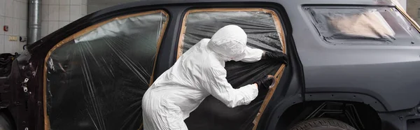 Arbeiterin in Handschuhen und Anzug klebt Klebeband auf Auto mit Zellophan in Garage, Banner — Stockfoto