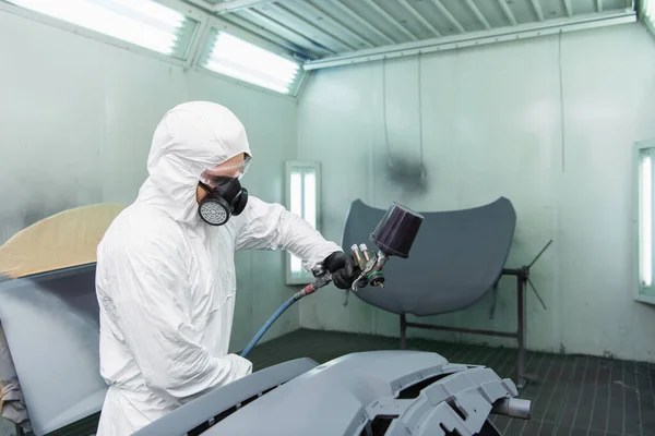 Young workman coloring car part with airbrush in garage — Stock Photo