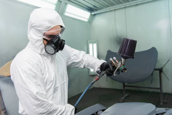 Workman in hazmat suit and goggles coloring car part in service — Stockfoto