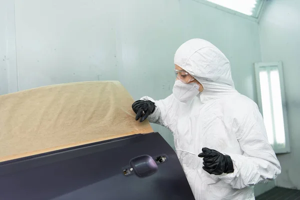 Workwoman en costume Hazmat travaillant avec la pièce de voiture dans le garage — Photo de stock