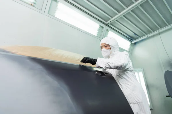 Femme de travail en lunettes et combinaison Hazmat travaillant avec la pièce de voiture en service — Photo de stock