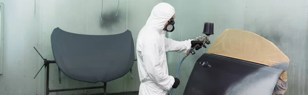 Workman in respirator and hazmat suit coloring car part in service, banner — Stock Photo