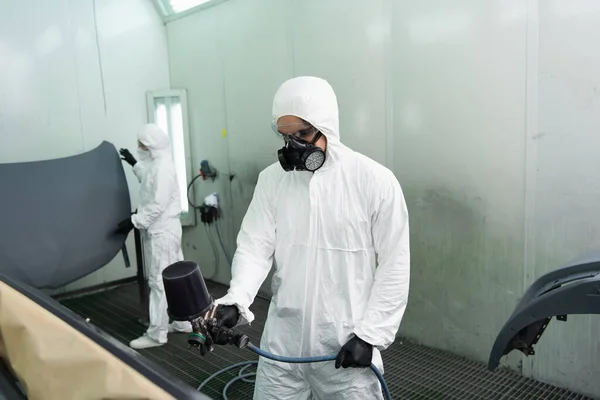 Ouvrier en uniforme de protection coloration floue pièce de voiture près de collègue en service — Photo de stock