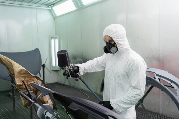 Молодий працівник тримає повітряну щітку під час фарбування частини автомобіля в гаражі — стокове фото