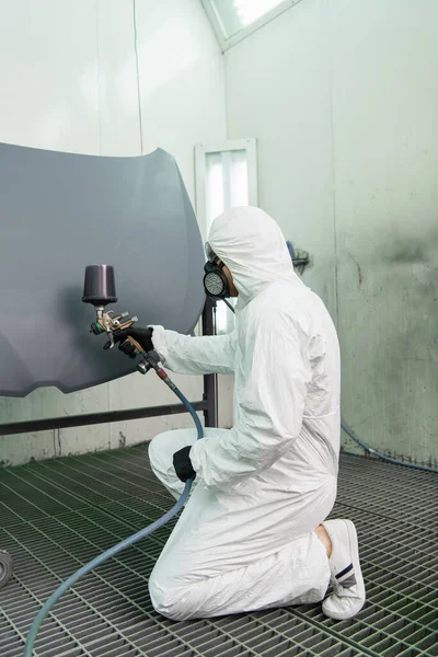 Side view of workman coloring car hood with airbrush in garage — Stock Photo