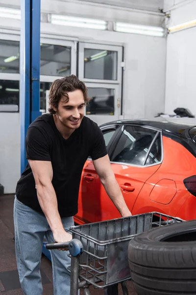 Smiling mechanic looking at tire on cart in car service — Stock Photo