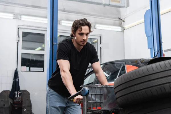 Mechanic standing near cart with tire in service — Stockfoto