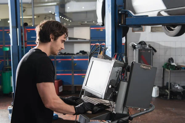 Seitenansicht des Mechanikers in Handschuhen mit dem Computer im Autoservice — Stockfoto