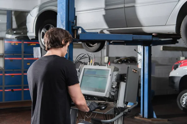 Workman using computer near auto in garage — Stockfoto