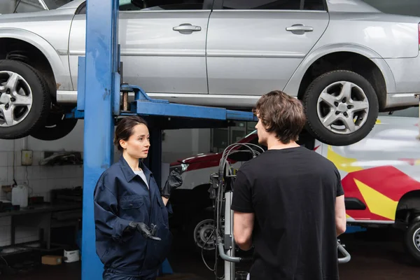 Workwoman pointing with fingers at car near colleague in garage — Stock Photo