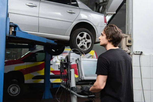 Vista laterale del lavoratore che guarda l'auto vicino al computer in garage — Foto stock