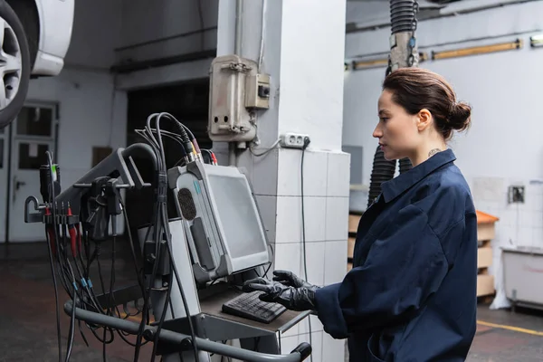 Side view of forewoman using computer near blurred car in garage — Stock Photo