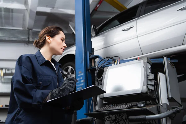 Side view of forewoman writing on clipboard near computer and car in garage — Foto stock