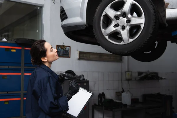 Young workwoman holding clipboard near car in service — Stock Photo