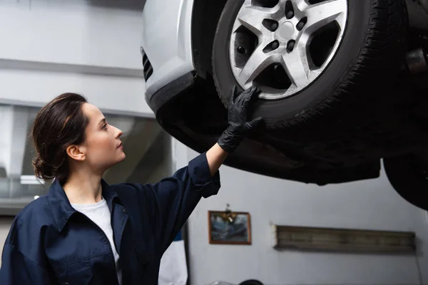 Vue latérale du mécanicien regardant la roue de la voiture en service — Photo de stock