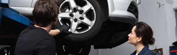 Young workman looking at car wheel near colleague in service, banner — стоковое фото