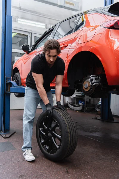 Workman in gloves changing tire near car in garage — Stock Photo