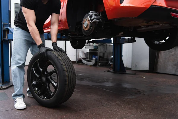 Cropped view of workman holding tire near auto in garage — Stock Photo