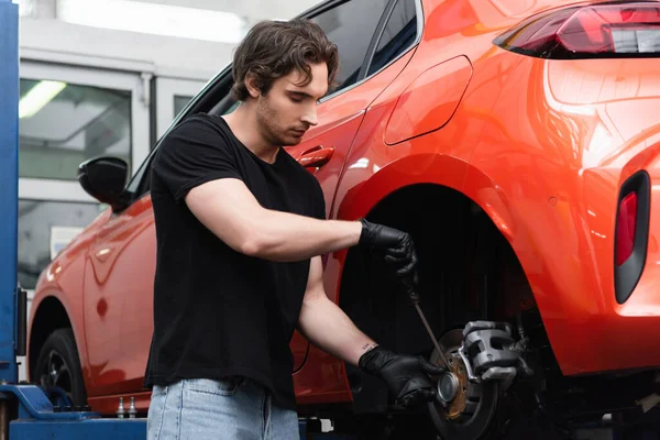 Jeune ouvrier travaillant avec tournevis et roue de voiture dans le garage — Photo de stock