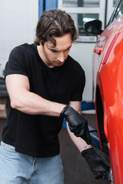 Workman in gloves working with screwdriver and car wheel in garage — стоковое фото