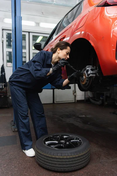 Side view of mechanic working with screwdriver and car wheel in garage — Stock Photo