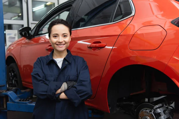 Young workwoman smiling at camera near car in garage — Stock Photo