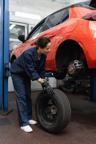 Mechanic holding tire near car in garage — стоковое фото
