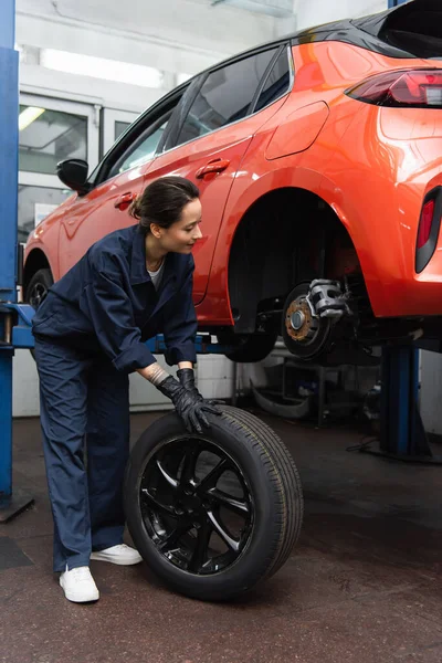 Smiling mechanic in gloves holding tire near auto — стоковое фото