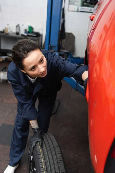 Young mechanic working with car and tire in garage — Stock Photo