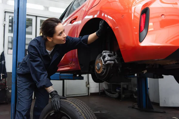 Workwoman in gloves checking car near tire in garage — стоковое фото