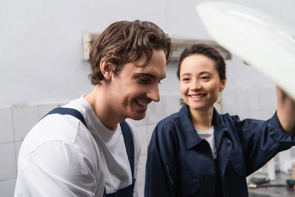 Cheerful mechanic standing near blurred colleague in garage — стоковое фото