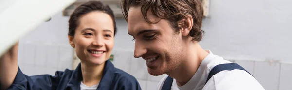 Positive mechanic standing near workwoman in car service, banner — стоковое фото