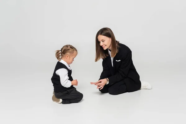 Cheerful mother showing fingers to child with down syndrome on grey — стоковое фото