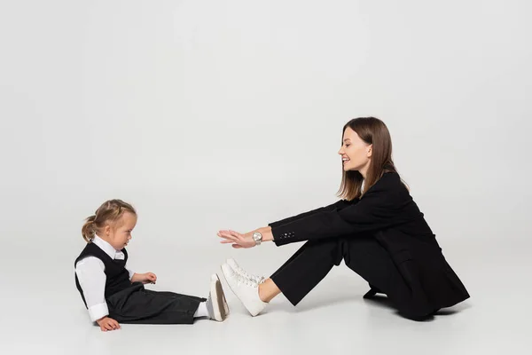 Side view of cheerful mother sitting and reaching child with down syndrome on grey — Fotografia de Stock