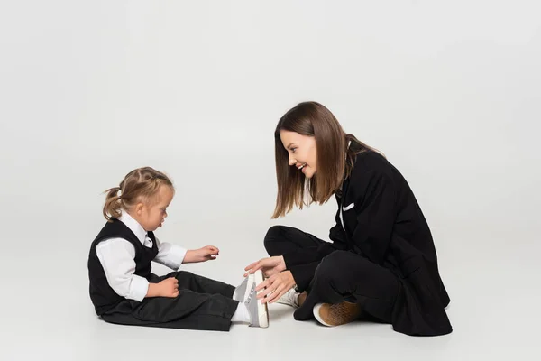 Side view of cheerful mother sitting near child with down syndrome on grey — стоковое фото