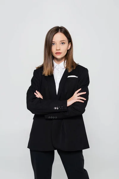 Stylish woman in suit standing with crossed arms isolated on grey — стоковое фото