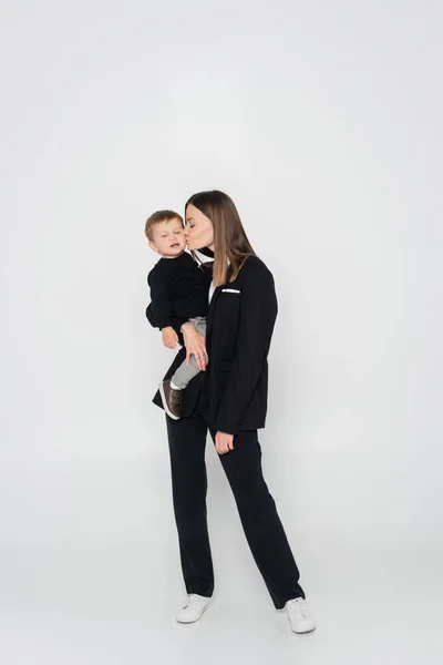 Повна довжина матері тримає в руках і цілує маленького сина на сірому — стокове фото
