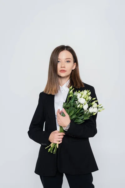 Trendy young woman in black suit holding flowers isolated on grey — стоковое фото