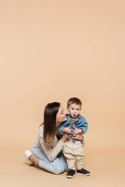 Happy mother hugging surprised toddler son on beige — Fotografia de Stock