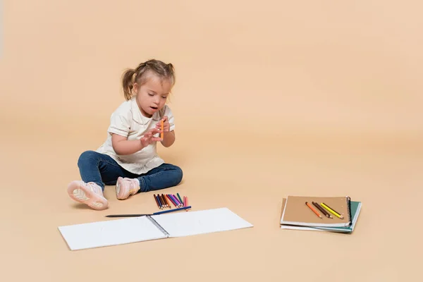 Child with down syndrome sitting near colorful pencils on beige — Photo de stock